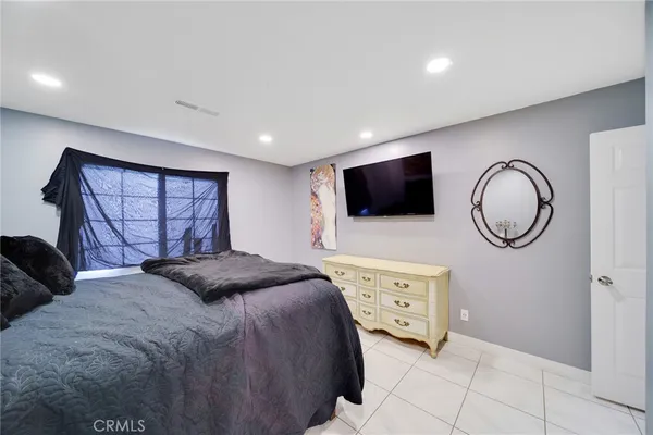 a bedroom with a bed a mirror on dresser and a flat screen tv