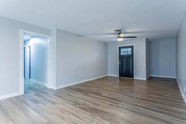 a view of an empty room with wooden floor and a ceiling fan