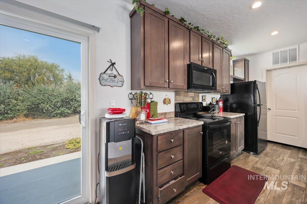 121 Sunset Drive North Hagerman, ID 83332 - Photo 11 of 31 Kitchen with dark brown cabinets, black appliances, dark wood finished floors, light countertops, and a textured ceiling
