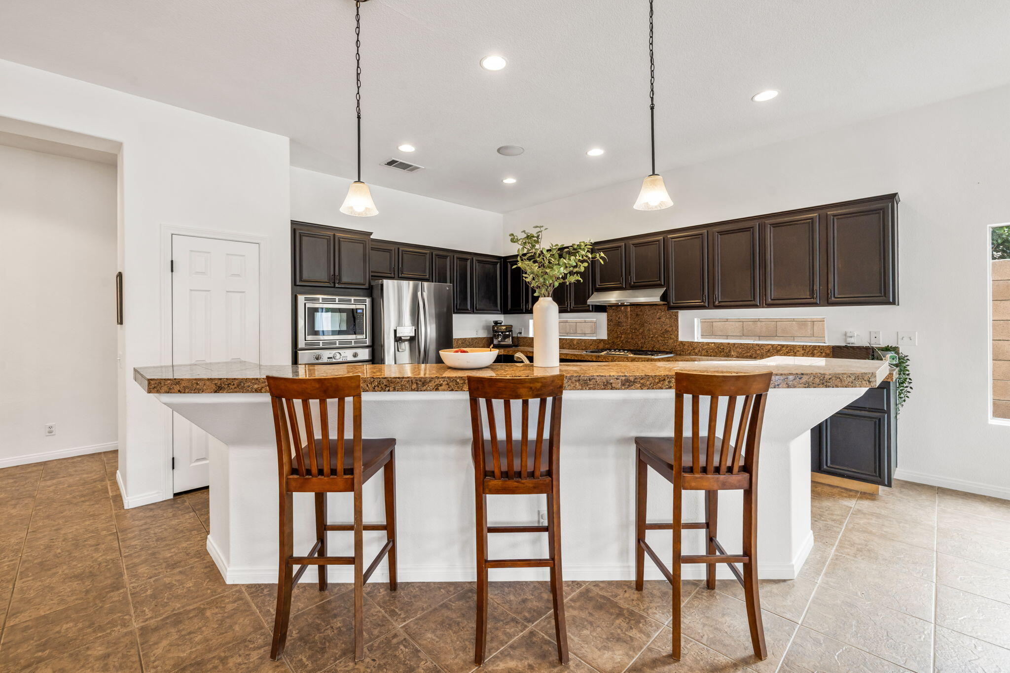 80543 Philadelphia Avenue Indio, CA 92201 - Photo 15 of 46 a kitchen with stainless steel appliances kitchen island granite countertop a dining table chairs and a refrigerator