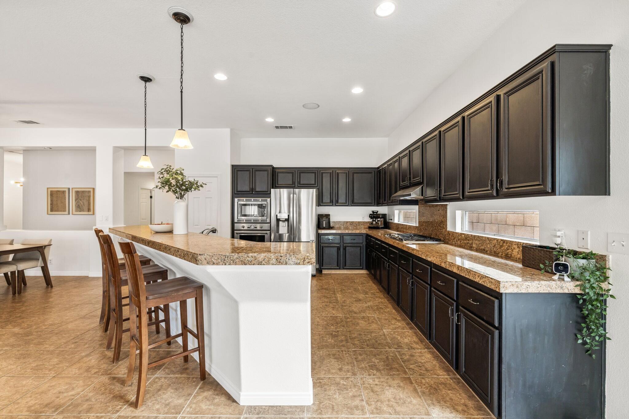 80543 Philadelphia Avenue Indio, CA 92201 - Photo 16 of 46 a kitchen with stainless steel appliances kitchen island granite countertop a stove top oven a sink a dining table and chairs