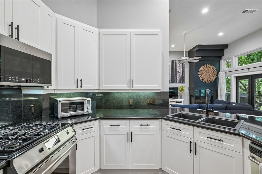 3553 Wheeler Street Dallas, TX 75209 - Photo 16 of 35 Kitchen with gas cooktop, white cabinetry, black granite counters, and open sightline to living room fireplace