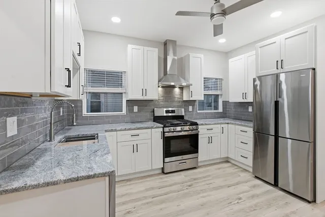 a kitchen with stainless steel appliances granite countertop a stove a sink dishwasher a refrigerator and white cabinets with wooden floor