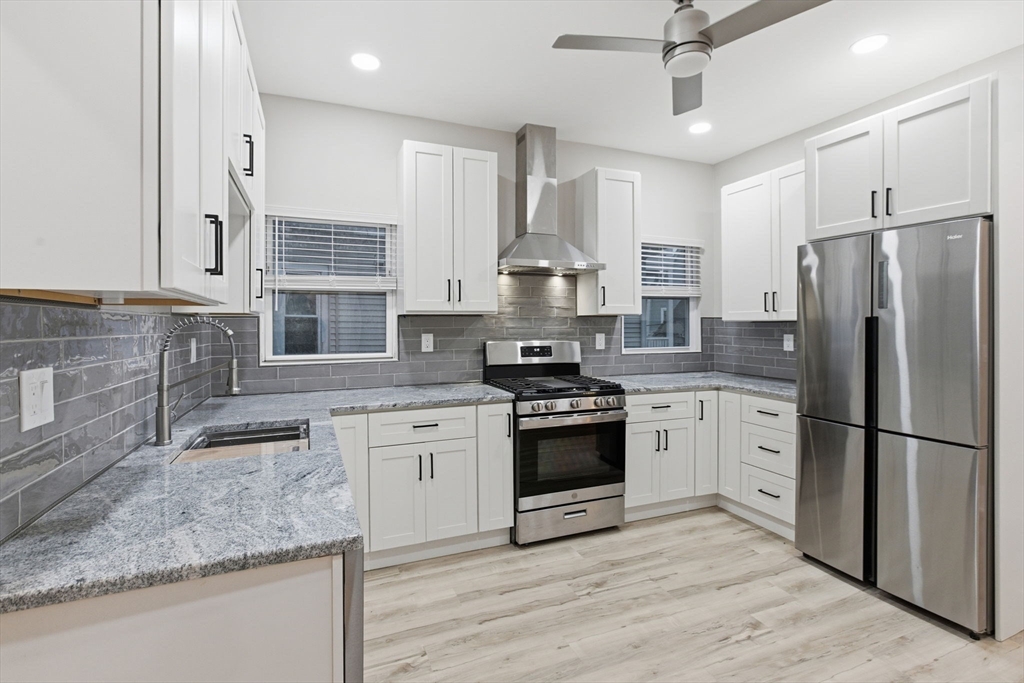 a kitchen with stainless steel appliances granite countertop a stove a sink dishwasher a refrigerator and white cabinets with wooden floor