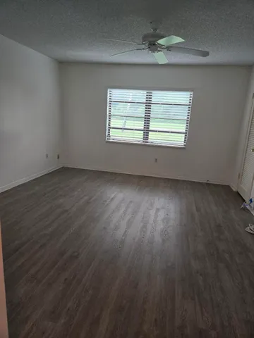 an empty room with wooden floor chandelier fan and windows