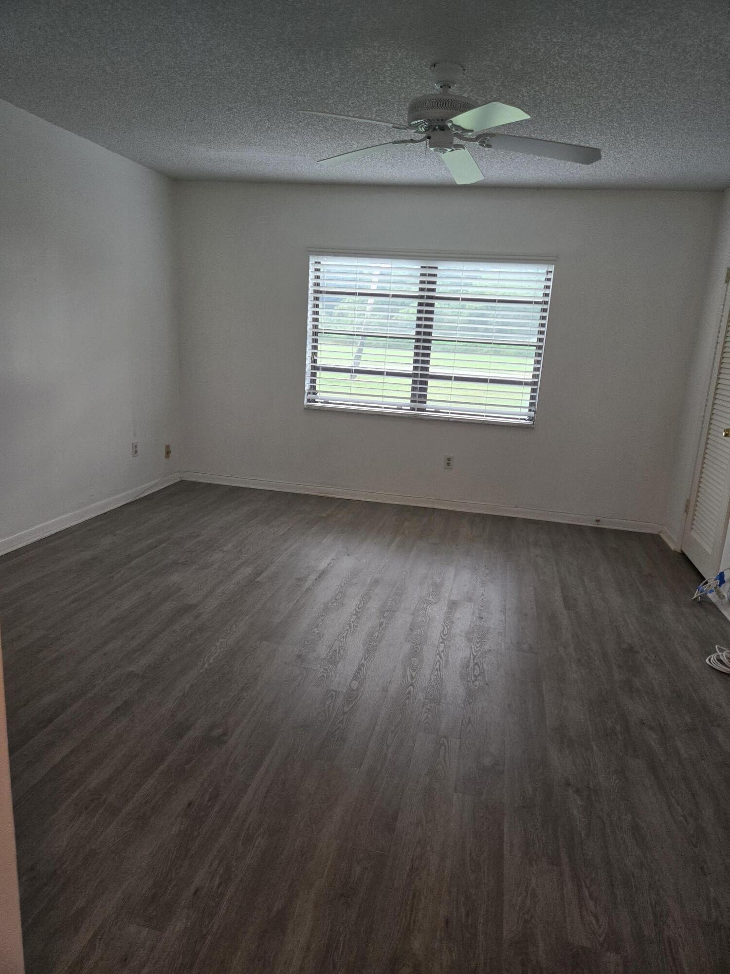 21213 Lago Circle, Unit G Boca Raton, FL 33433 - Photo 7 of 8 an empty room with wooden floor chandelier fan and windows