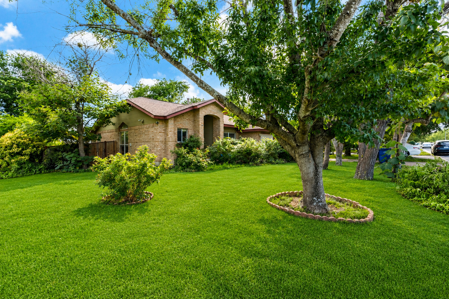 5611 Meadow Crest Austin, TX 78744 - Photo 1 of 29 A traditional brick home is nestled amidst lush green landscaping and mature trees, creating a serene environment.