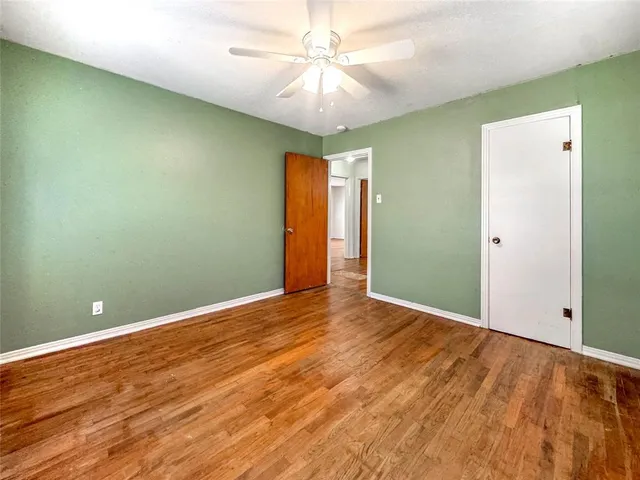 an empty room with a chandelier fan and wooden floor