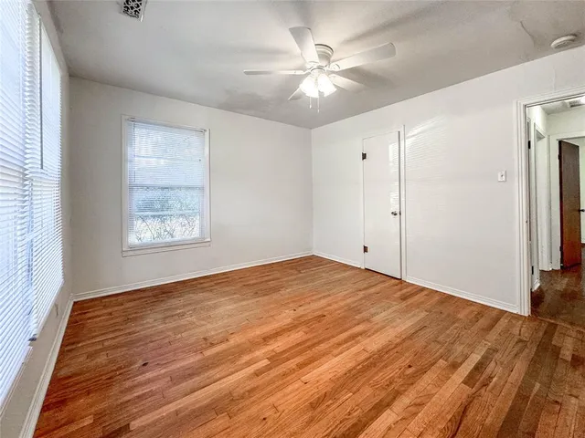 an empty room with wooden floor chandelier fan and windows