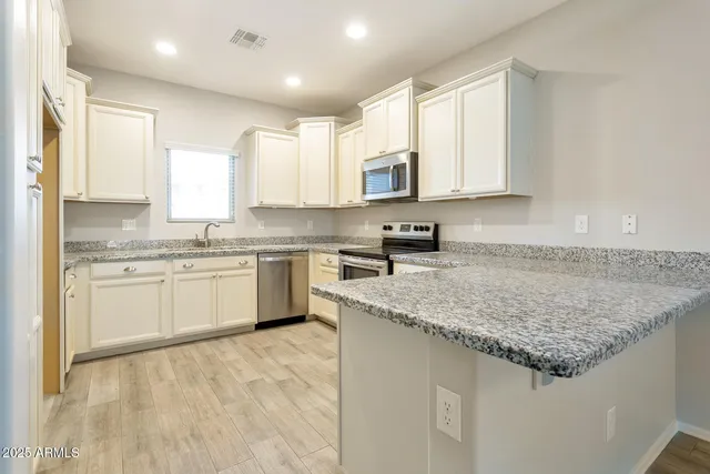 a kitchen with stainless steel appliances granite countertop a sink dishwasher a stove and white cabinets with wooden floor