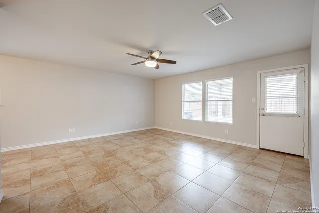 an empty room with chandelier fan and windows