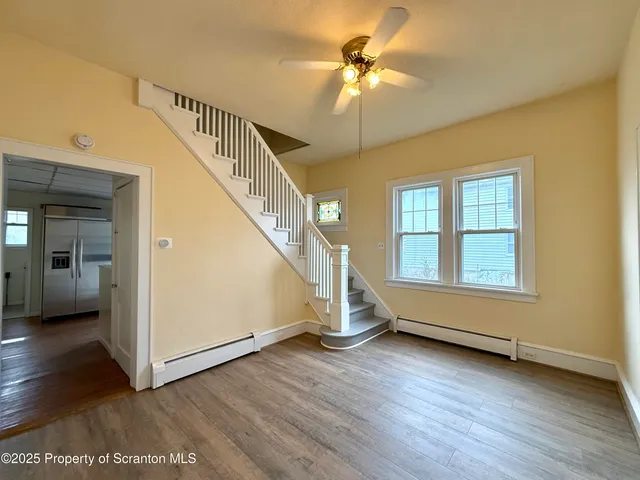 a view of an empty room with wooden floor and a ceiling fan