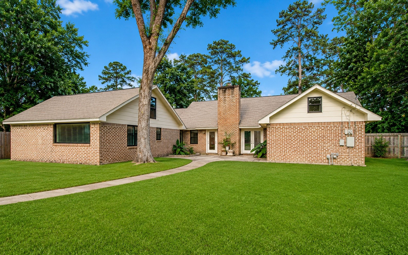 1801 Benbow Way Houston, TX 77080 - Photo 29 of 32 This photo shows a charming single-story brick house with a gabled roof, surrounded by a lush green lawn. The home features a prominent central chimney and a clean, well-maintained exterior. A paved walkway leads to the entrance, and mature trees provide a serene backdrop.