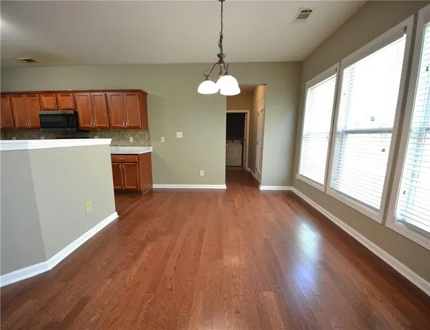 a view of an empty room with window wooden floor and kitchen