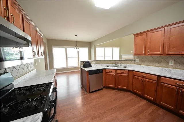 a kitchen with stainless steel appliances granite countertop a stove a sink dishwasher and wooden cabinets with wooden floor