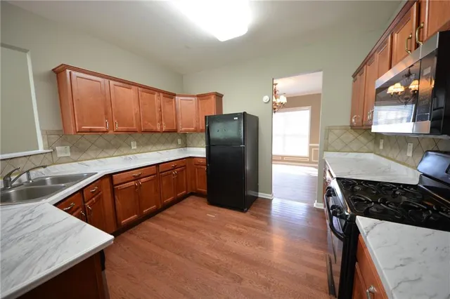 a kitchen with stainless steel appliances granite countertop a refrigerator a stove and a sink with wooden cabinets