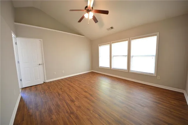 an empty room with wooden floor chandelier fan and windows