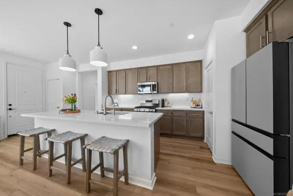 a kitchen with granite countertop a refrigerator a sink dishwasher a stove and white cabinets with wooden floor