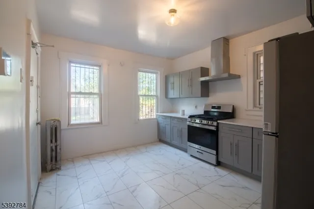 a kitchen with stainless steel appliances granite countertop a refrigerator a sink dishwasher a stove and white countertops with wooden floor