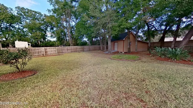 a view of a backyard with large trees and wooden fence