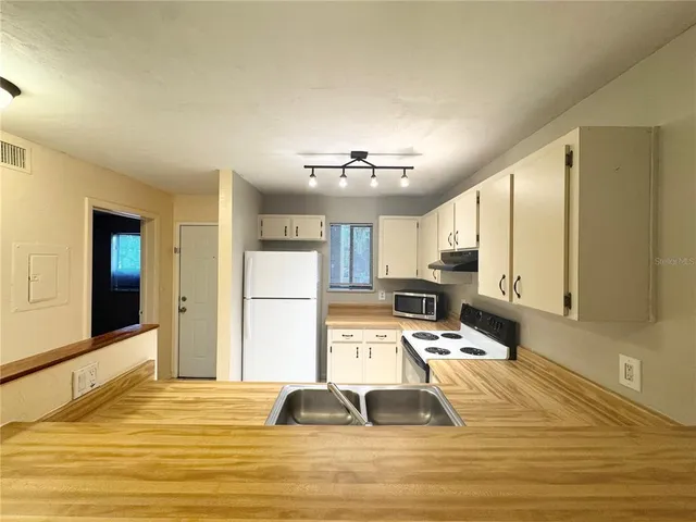 a view of a kitchen with kitchen island a counter top space a sink wooden floor and a refrigerator