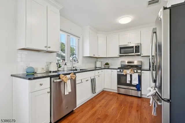 a kitchen with stainless steel appliances granite countertop a refrigerator a stove top oven a sink and dishwasher with wooden floor