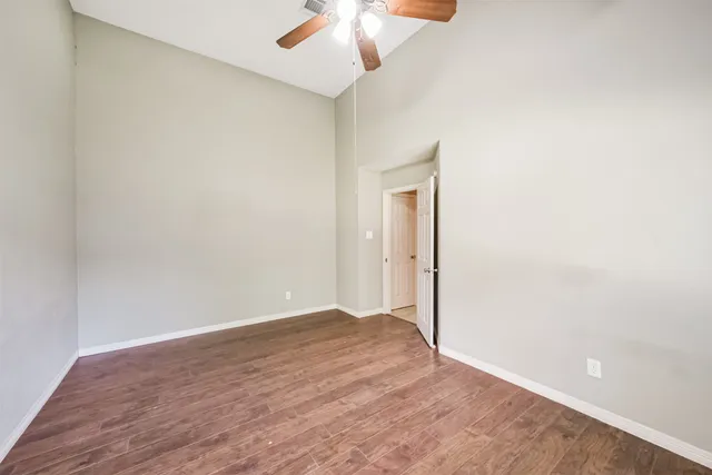 an empty room with wooden floor fan and windows
