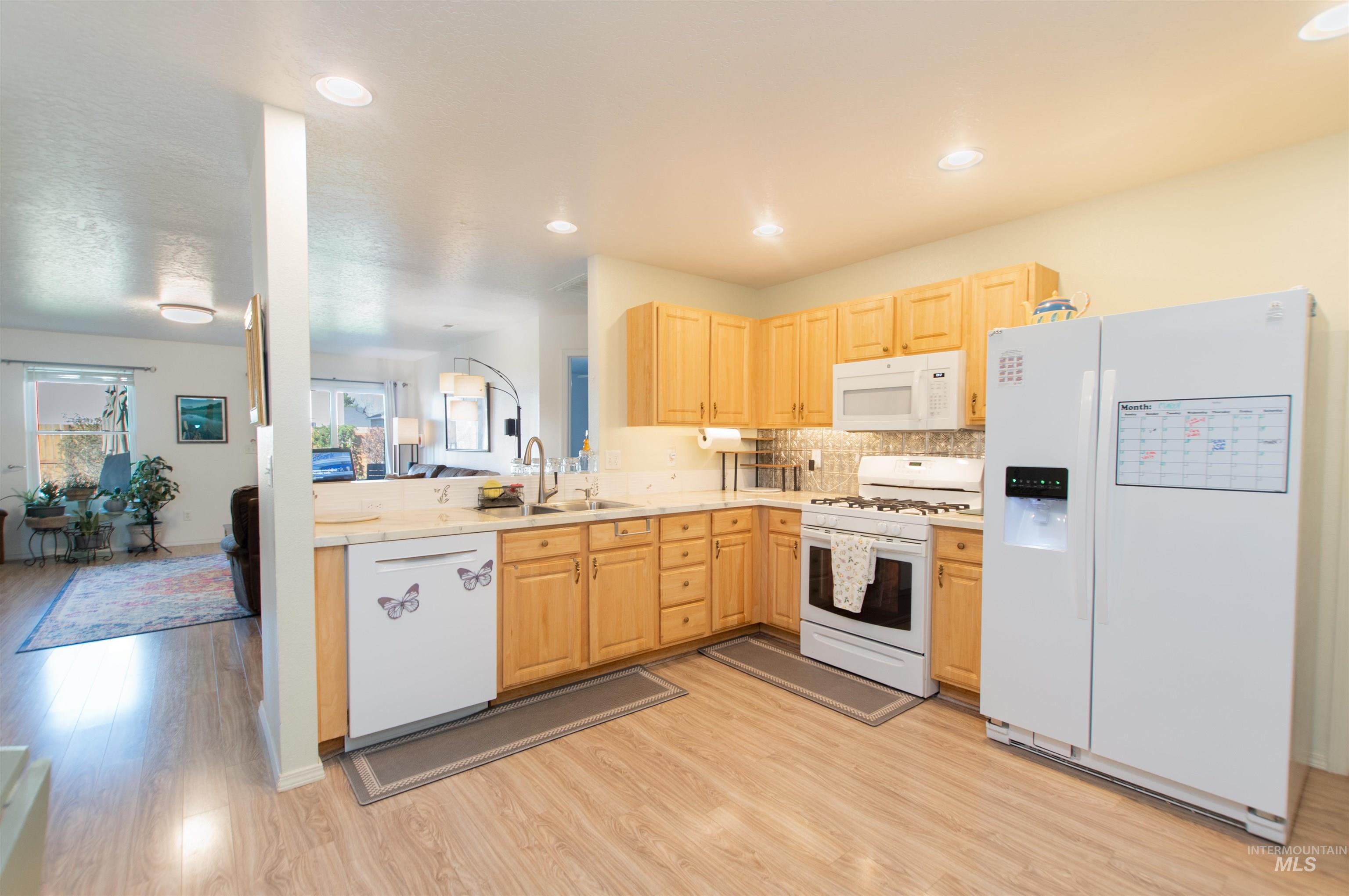 16711 Abram Avenue Caldwell, ID 83607 - Photo 5 of 24 Kitchen featuring light wood finish cabinetry, white appliances, light countertops, light wood-type flooring, and decorative backsplash