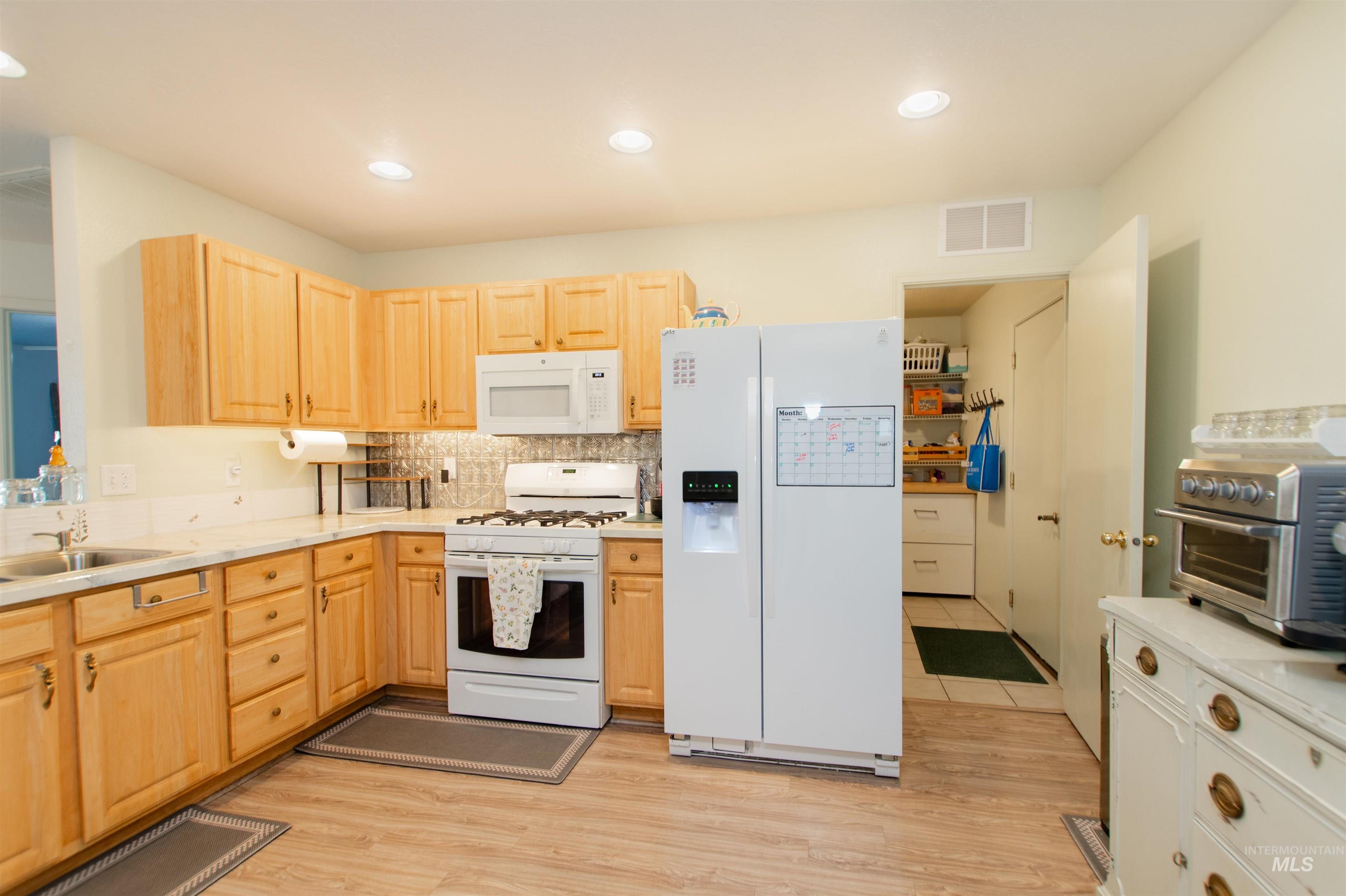 16711 Abram Avenue Caldwell, ID 83607 - Photo 6 of 24 Kitchen with light wood finish cabinets, white appliances, light countertops, light wood finished floors, and recessed lighting