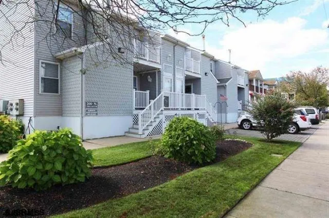 a view of a white house next to a yard with potted plants and large trees