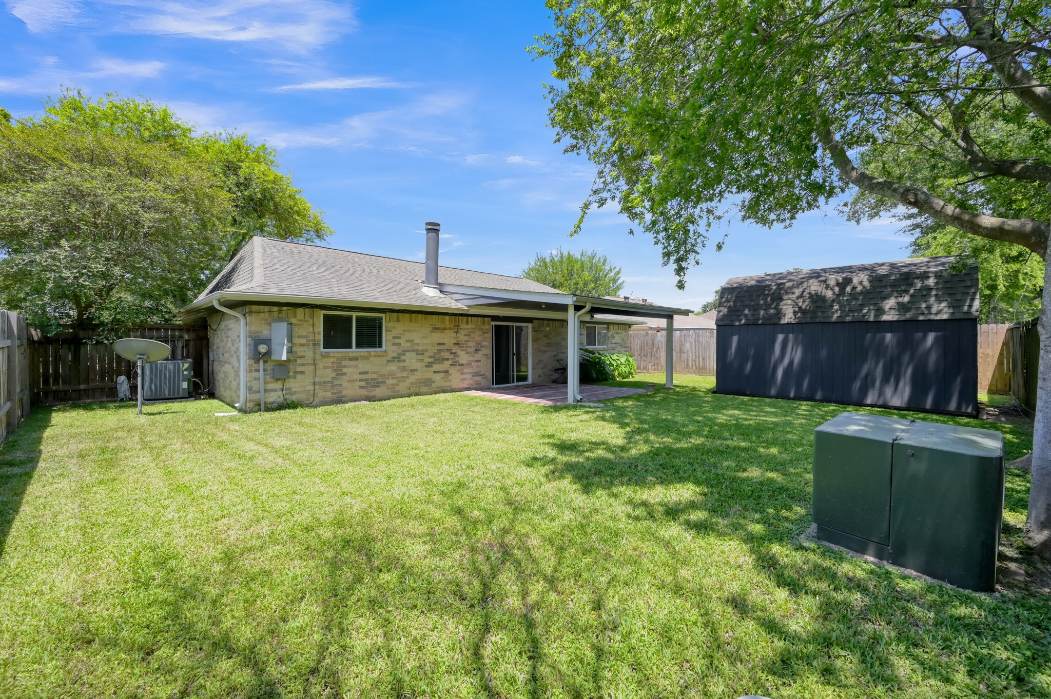 12015 Fallbrook Drive Houston, TX 77065 - Photo 27 of 29 This backyard features a spacious lawn, mature trees, a covered patio for outdoor relaxation, and a large storage shed. It's enclosed by a wooden fence, providing privacy and a safe space for activities.