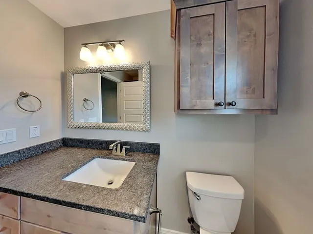 a bathroom with a granite countertop sink and a toilet