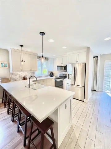 a kitchen with stainless steel appliances kitchen island a table chairs in it white cabinets and wooden floors