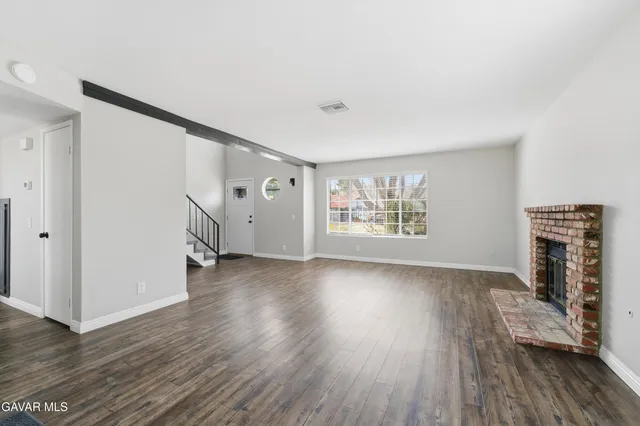 an empty room with wooden floor fireplace and windows