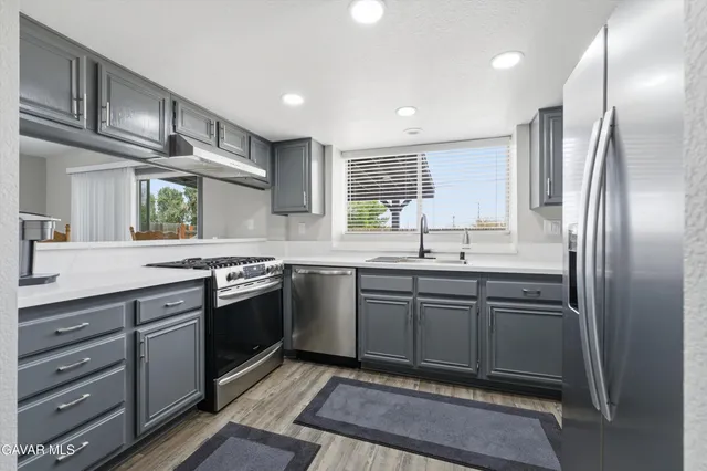 a kitchen with stainless steel appliances granite countertop a sink a stove a refrigerator cabinets and a window