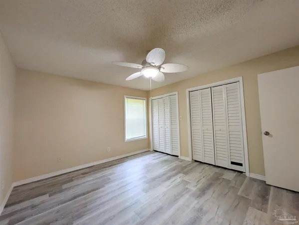 an empty room with wooden floor chandelier fan and windows