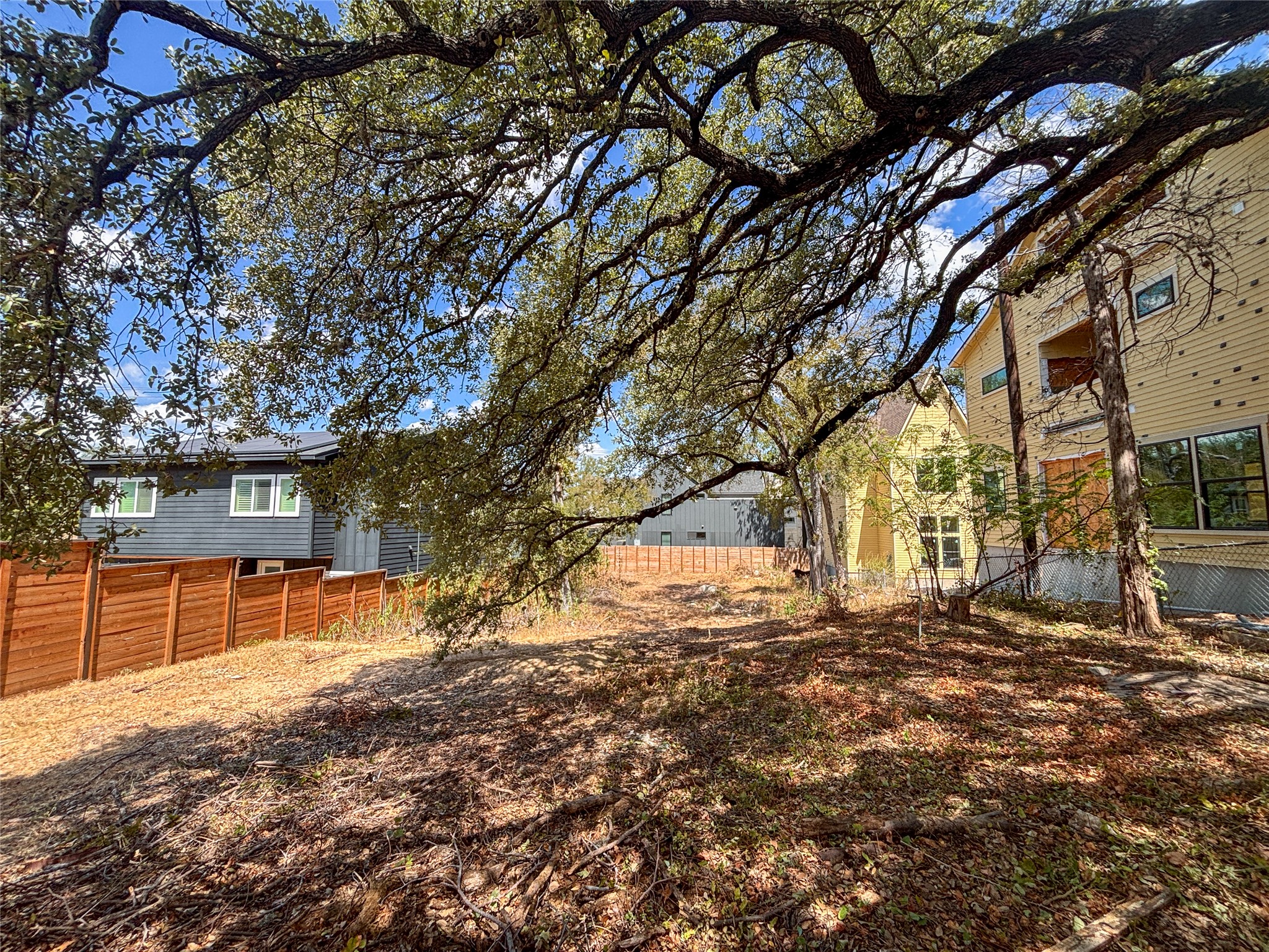 4602 Santa Anna Street Austin, TX 78721 - Photo 12 of 14 Mature shade trees canopy a spacious sloped lot bordered by wood fencing.
