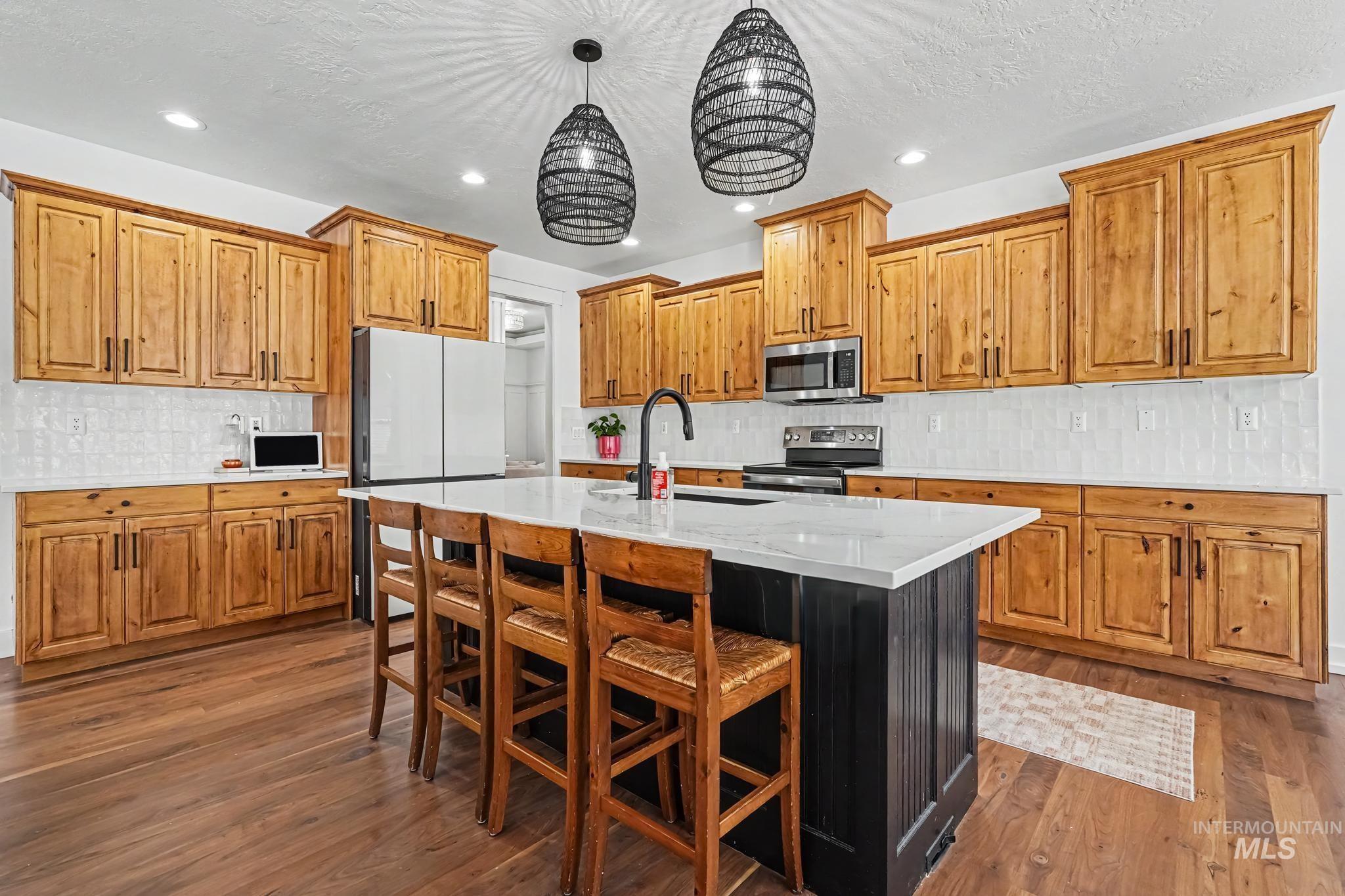 2340 South Alaska Way Meridian, ID 83642 - Photo 7 of 48 Kitchen with wood-finish flooring, natural wood cabinetry, white subway tile backsplash, and a center island with a white countertop