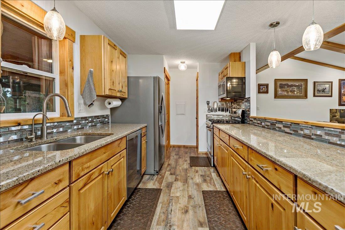 79 Sunset Loop Cascade, ID 83611 - Photo 10 of 44 Kitchen featuring wood-finish flooring, natural wood cabinetry, light-toned countertops, a glass tile backsplash, and stainless steel appliances