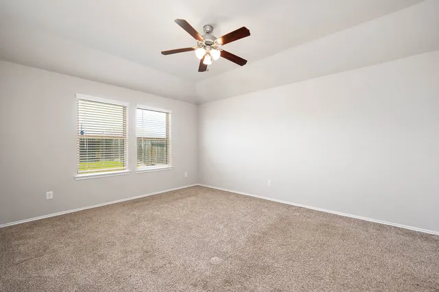 an empty room with ceiling fan and windows
