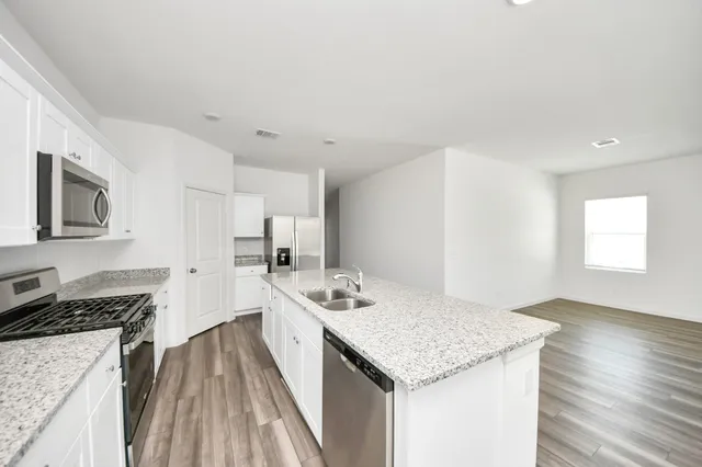 a kitchen with granite countertop a stove top oven a sink dishwasher and white cabinets with wooden floor