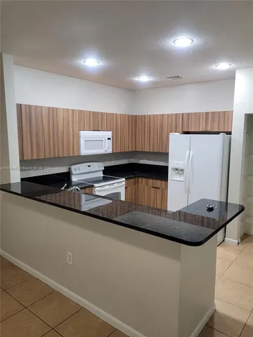 a kitchen with granite countertop a refrigerator a stove and wooden cabinets