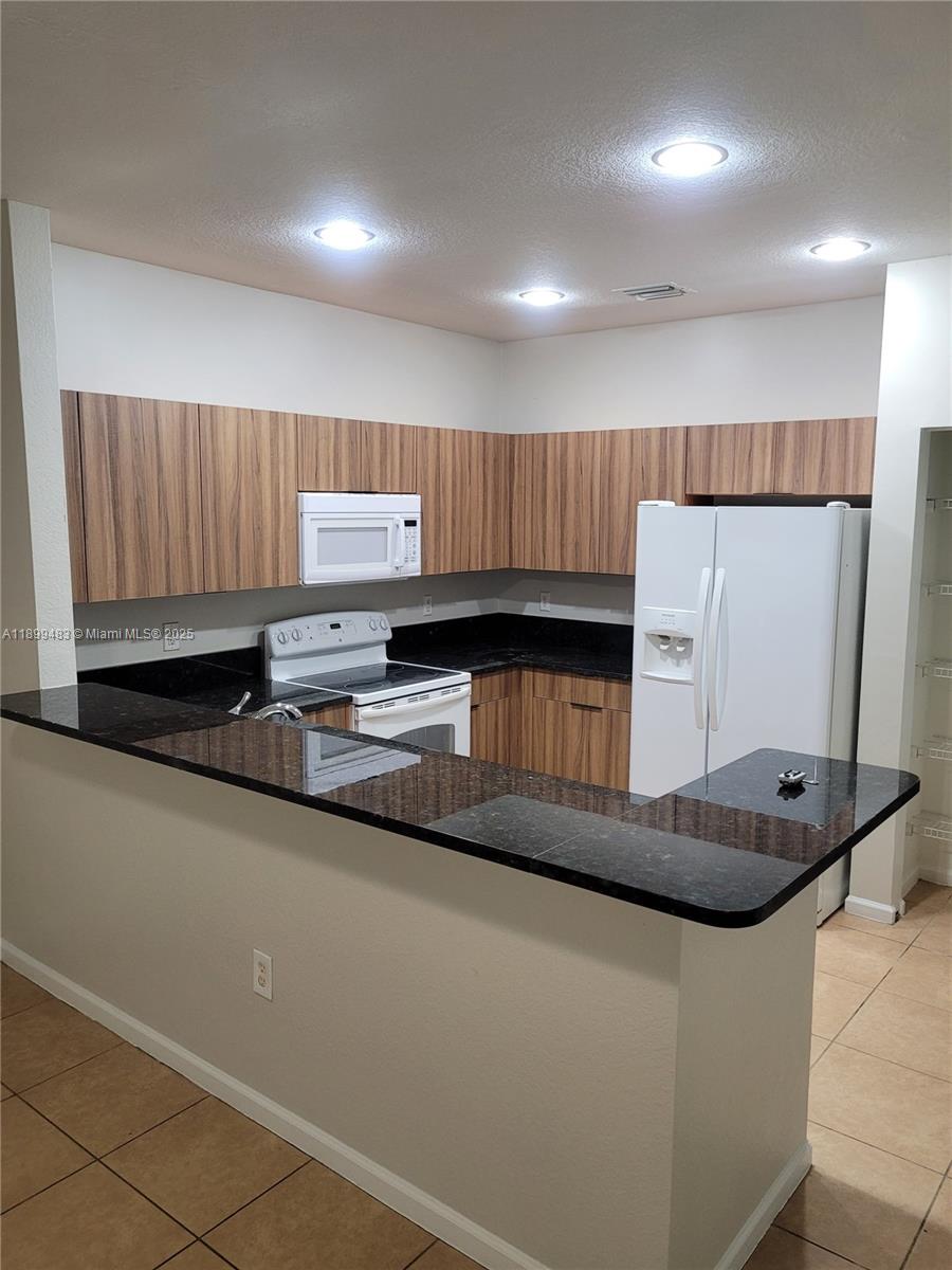 2556 Southwest 83rd Avenue, Unit 101 Miramar, FL 33025 - Photo 6 of 19 a kitchen with granite countertop a refrigerator a stove and wooden cabinets