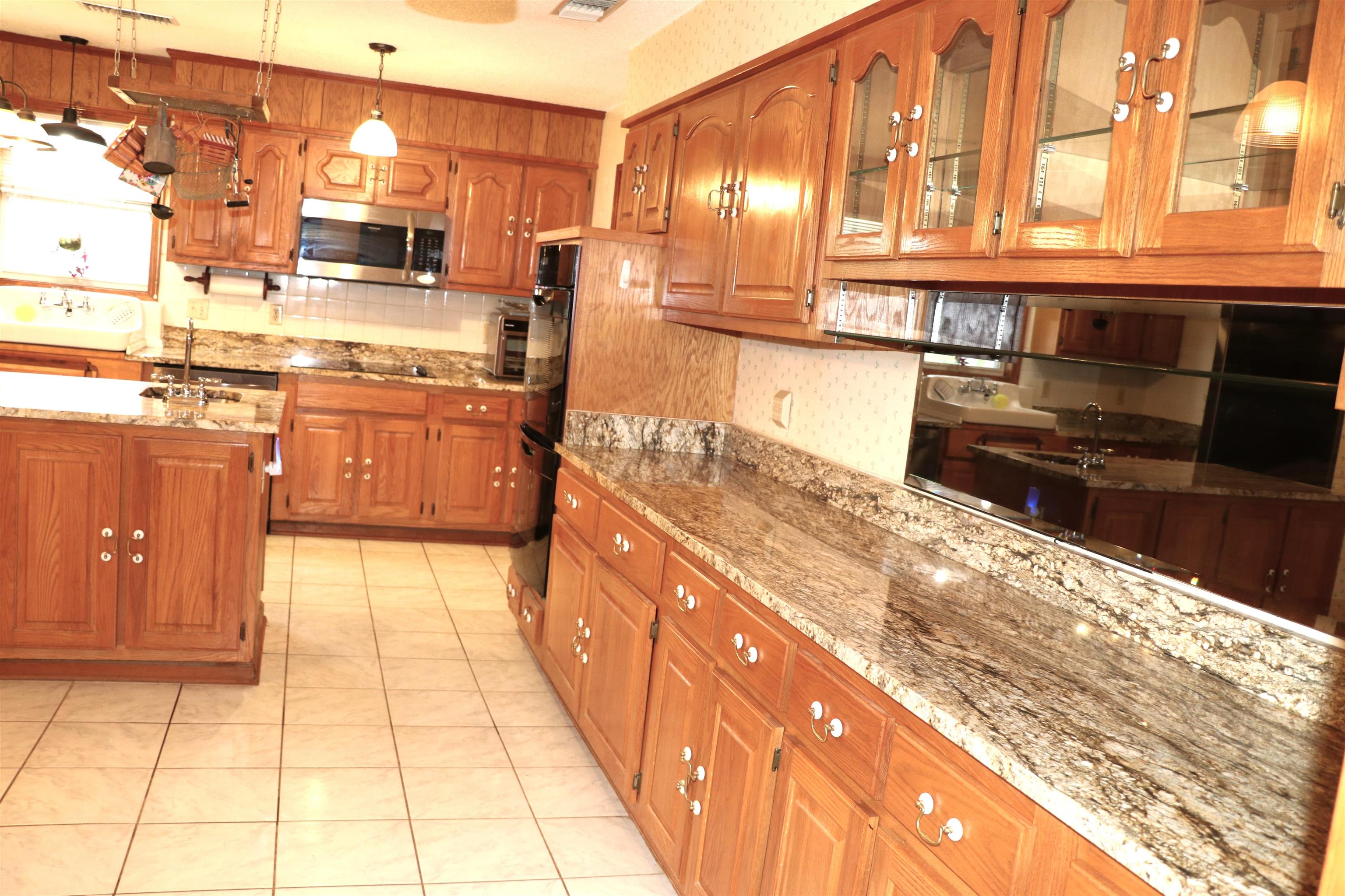 937 Kelleys Chapel Road Burlison, TN 38015 - Photo 10 of 40 Spacious kitchen featuring extensive wood cabinetry, patterned stone countertops, stainless steel appliances, a tiled backsplash, and an integrated island with a sink