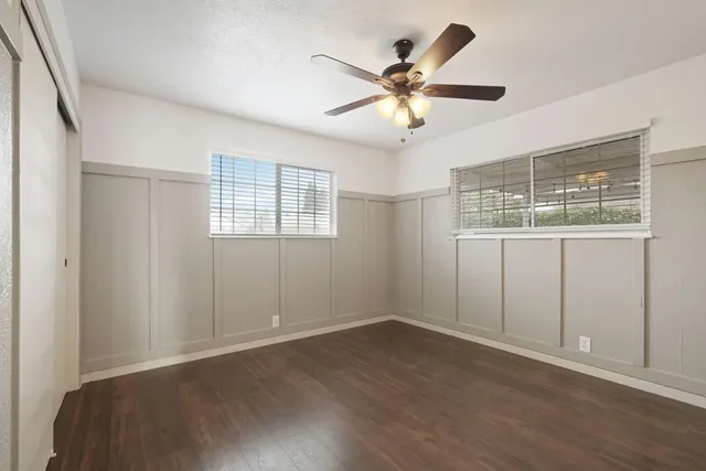an empty room with wooden floor fan and windows