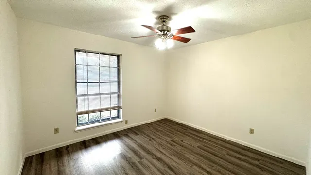 an empty room with wooden floor fan and windows