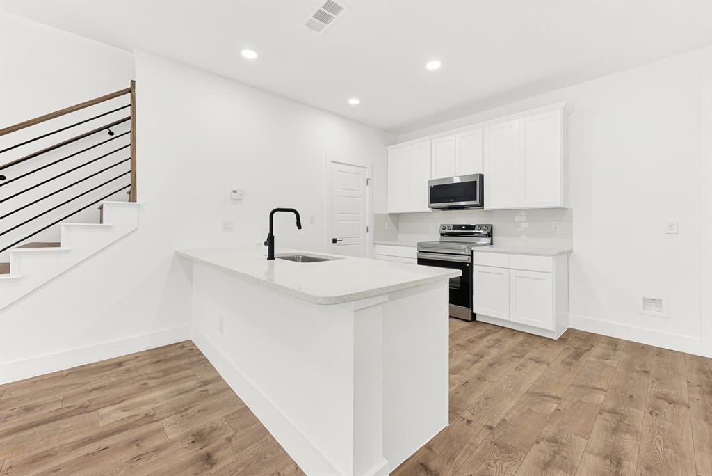 9471 Timberleaf Drive Dallas, TX 75243 - Photo 13 of 39 Modern kitchen featuring an island with a matte black faucet, stainless steel appliances, white cabinetry, recessed lighting, and wood-finish flooring