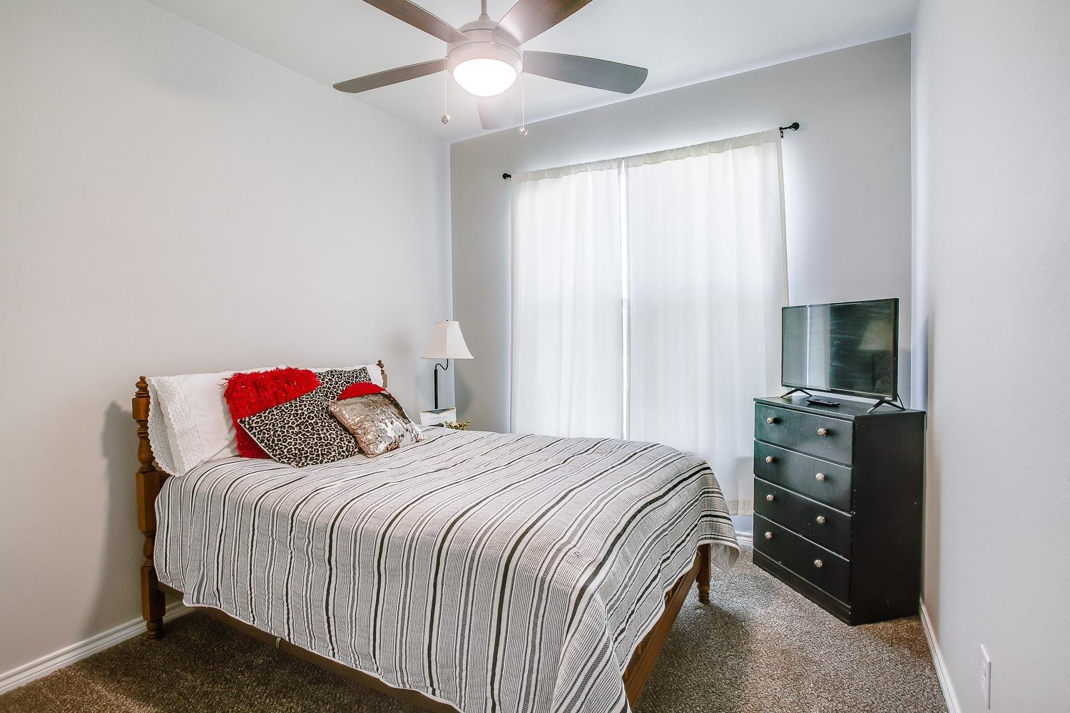 7017 10th Street Lubbock, TX 79416 - Photo 9 of 16 a bedroom with a bed and a flat tv screen on a dresser