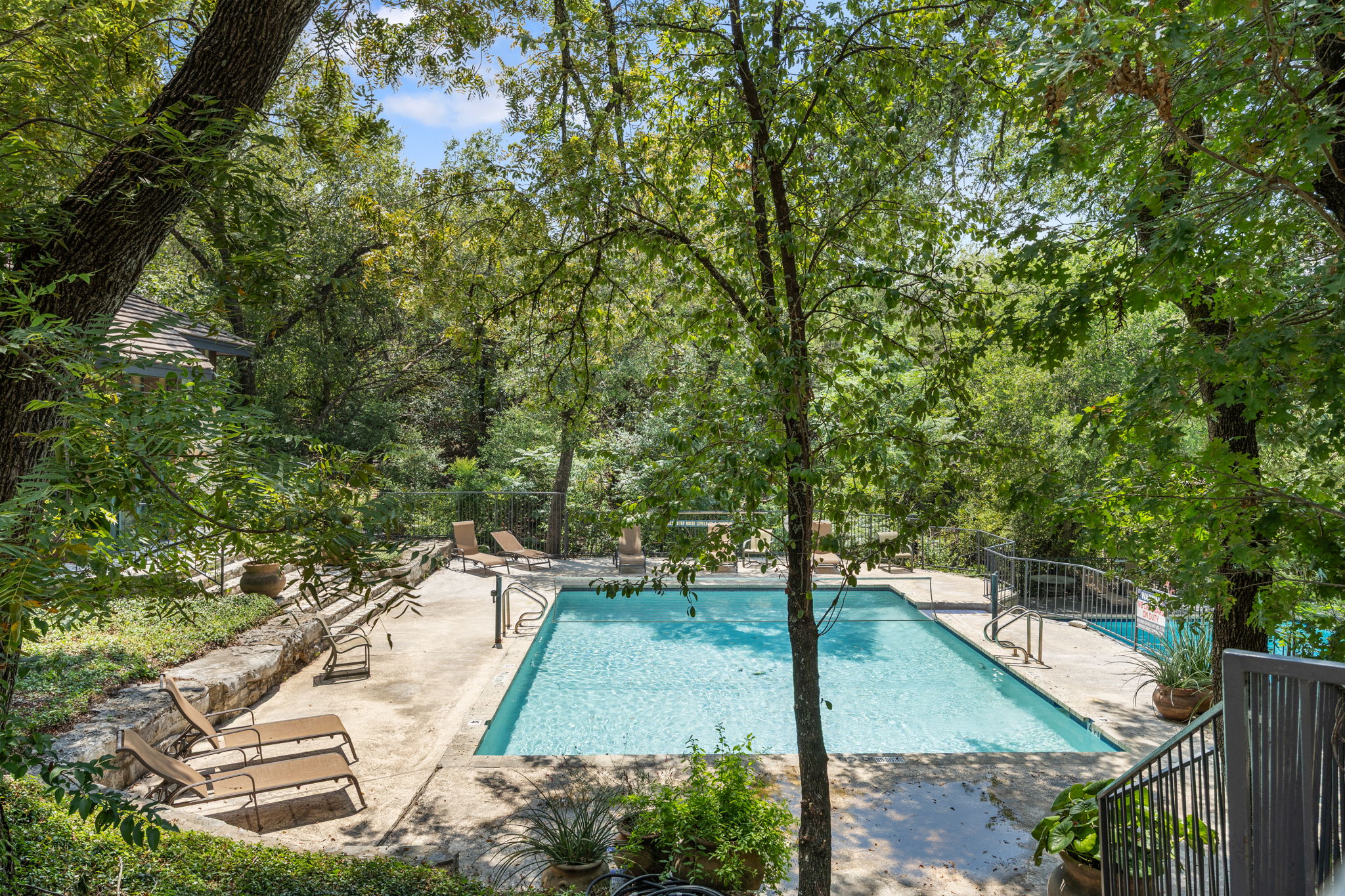 4711 Spicewood Springs Road, Unit 1106 Austin, TX 78759 - Photo 18 of 19 Outdoor swimming pool featuring a concrete surround, stone retaining wall, and lush perimeter landscaping
