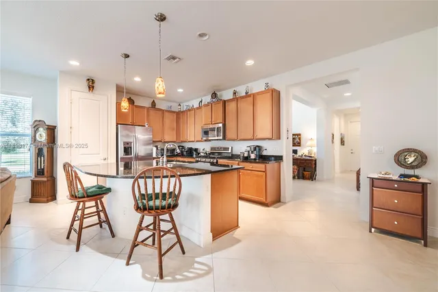 a kitchen with stainless steel appliances kitchen island granite countertop a stove a sink a refrigerator cabinets and a dining table